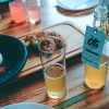 open bottle of kombucha next to a half-filled glass, with food in the background