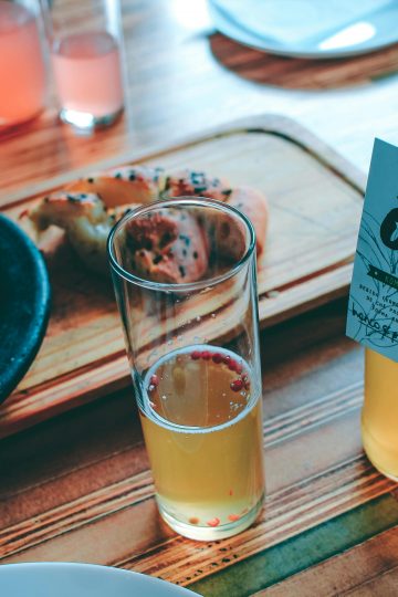 open bottle of kombucha next to a half-filled glass, with food in the background